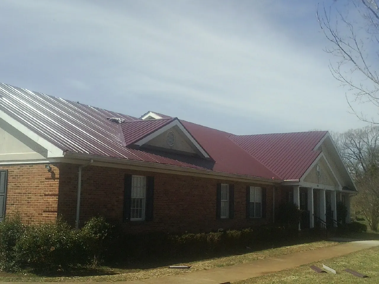 Red metal roof with gabled entries on a long brick building, from a Hail Damage Roof Repair job in Orbisonia