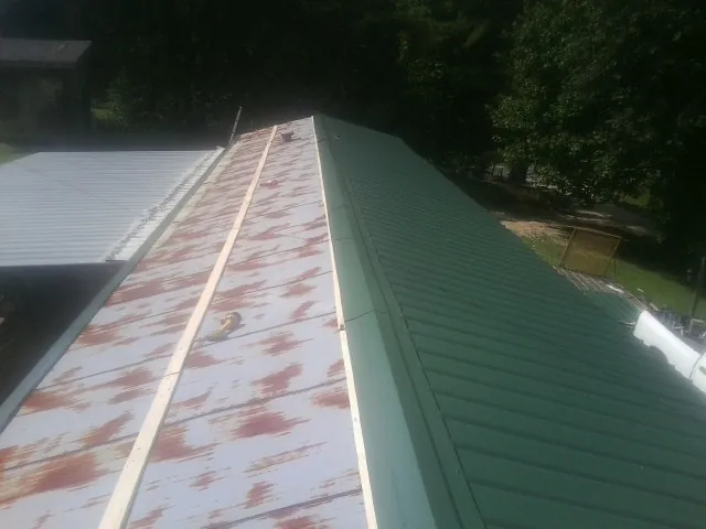 Old rusted panels beside newly installed green metal roofing — Wind Damage Roof Repair by Roofing Brothers in Orbisonia