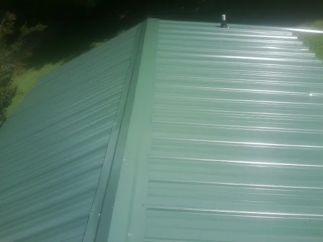 New green metal panels meeting at the ridge of a roof — Flat Roof Repair work by our crew in Orbisonia