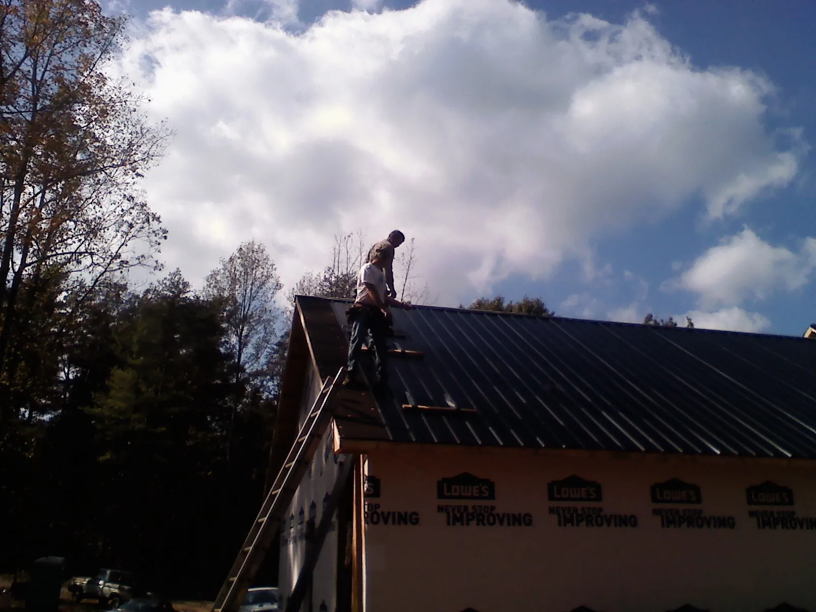 Roofer fastening dark metal panels high against a cloudy sky, from a Roof Inspection job in Orbisonia