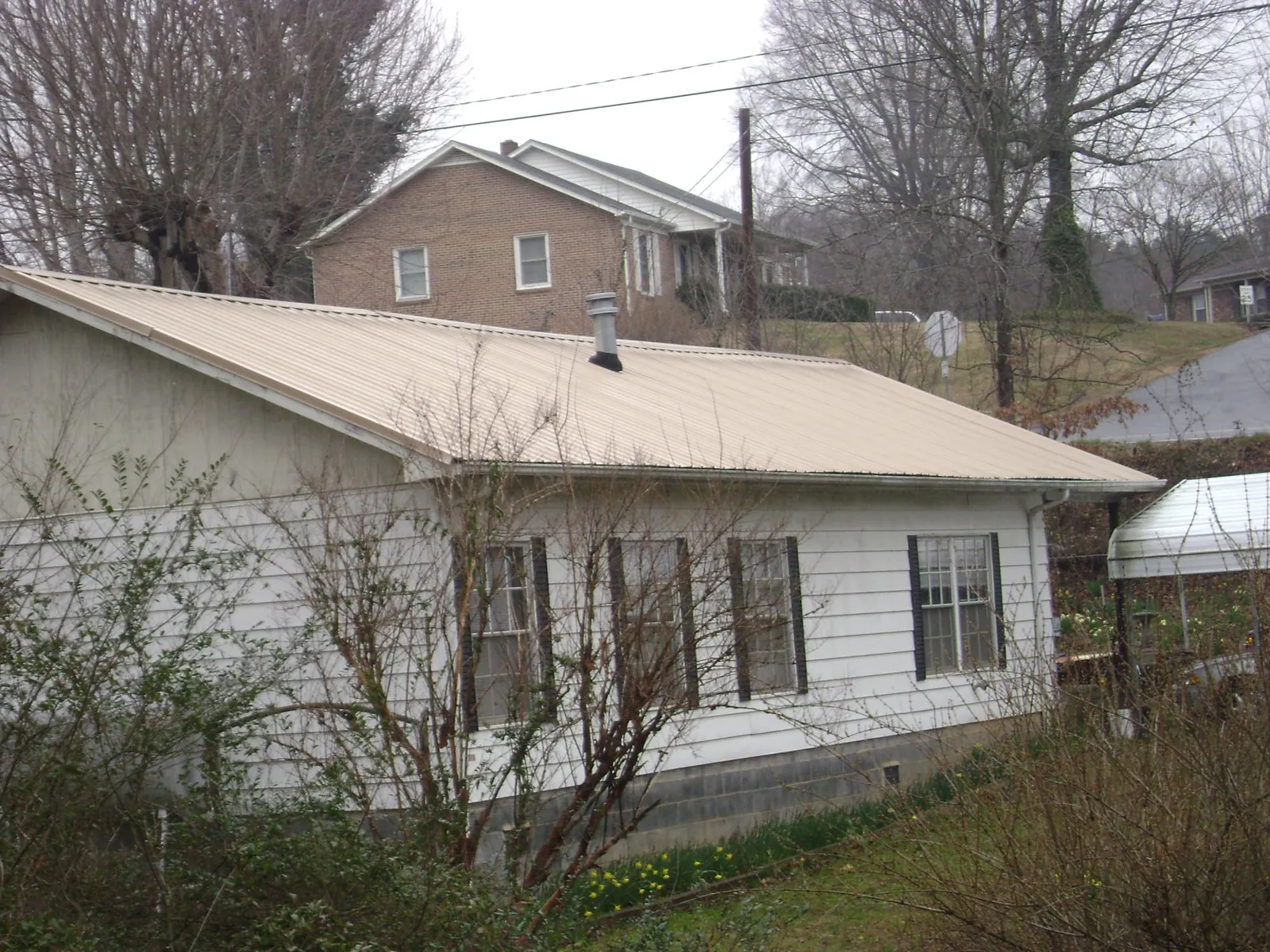 Tan metal roof on a white sided house set into a hillside — Commercial Roofing by Roofing Brothers in Orbisonia