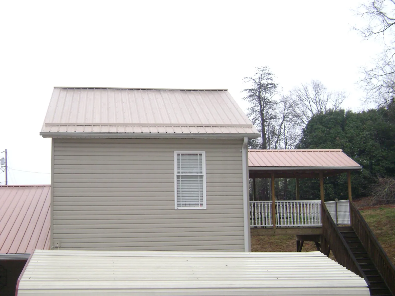 Tan metal roofs on a two story addition and attached porch, from a Roof Replacement job in Orbisonia